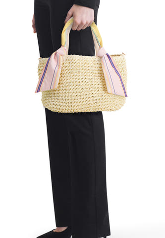 Sac à bandoulière tissé écru de PIECES® avec des foulards rayés colorés aux anses, porté avec un pantalon et des chaussures noirs.