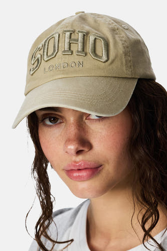 Casquette écru de PIECES, brodée de 'Soho London', portée par un mannequin, gros plan.