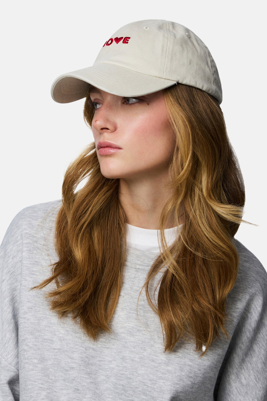 Casquette blanche de PIECES, avec texte rouge "Love" sur le devant, portée par un mannequin avec un pull gris.
