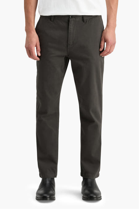 Grijze chino van SCOTCH & SODA, gedragen met zwarte schoenen en een wit shirt, vooraanzicht.
