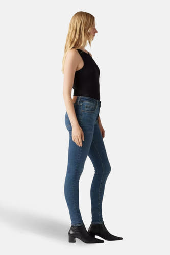Skinny jeans van donkerblauw denim van Levi's, gedragen met een zwarte top en laarzen met hak, in zijaanzicht.
