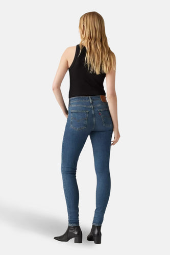 Skinny jeans in donkerblauw denim van Levi's, gezien van achteren, met zwarte tanktop en zwarte laarsjes.
