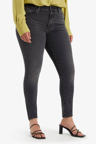 Skinny jeans van donkergrijs denim van Levi's, gedragen met een geel overhemd en zwarte hakken, in een close-up.
