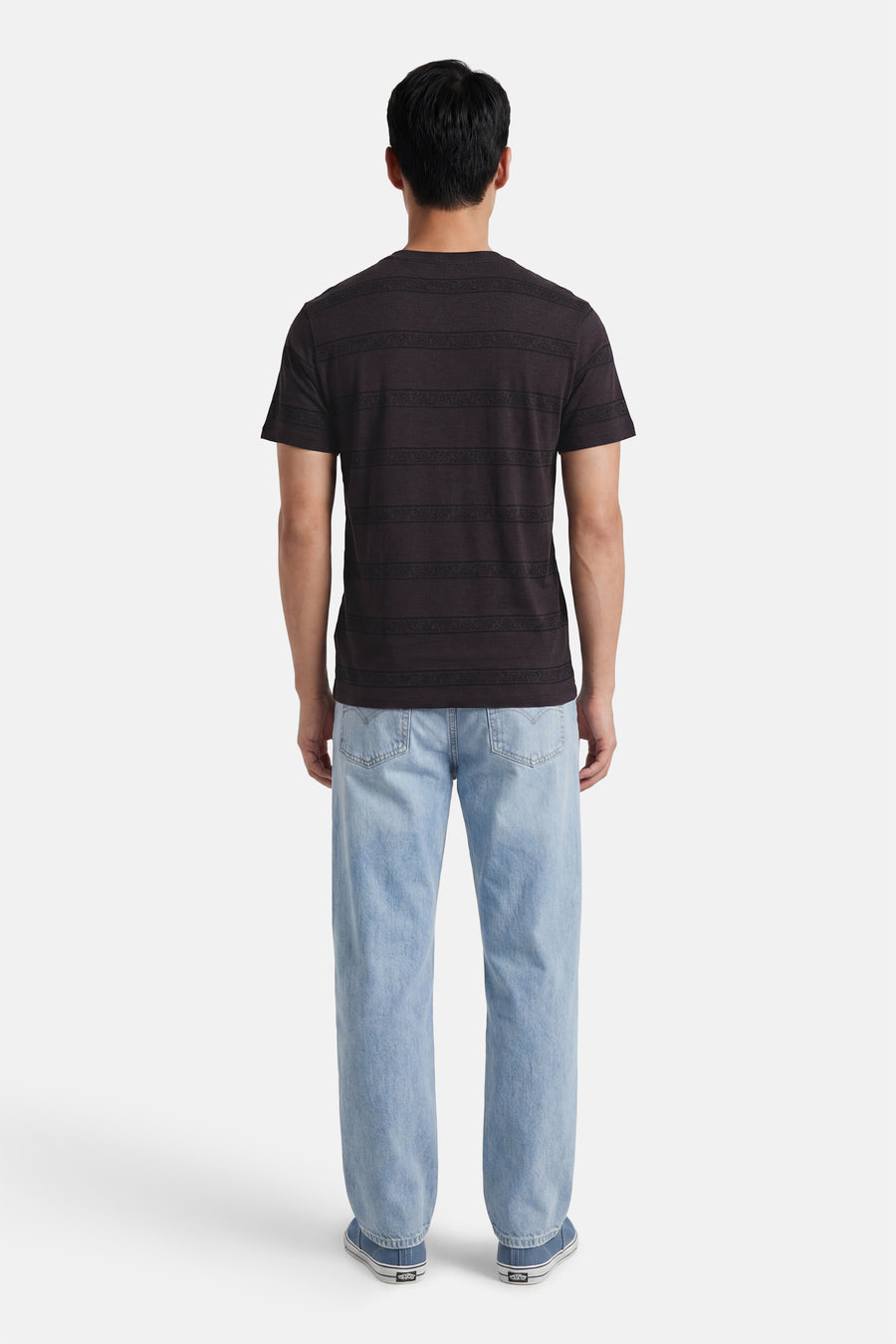 Zwart T-shirt met korte mouwen van Levi's® met horizontale banden en patronen, gedragen door een man, achterkant, met lichte spijkerbroek en blauwe sneakers.