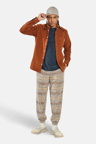 Oranje corduroy overhemd met lange mouwen van REDEFINED REBEL, gedragen met een muts en gestreepte broek.
