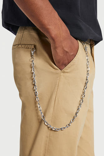 Beige broek van REDEFINED REBEL met zilverkleurige broekketting, steekzak en hand in de zak.
