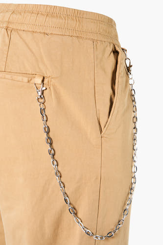 Beige broek van REDEFINED REBEL met zilverkleurige ketting aan de zijkant en elastische tailleband, close-up.
