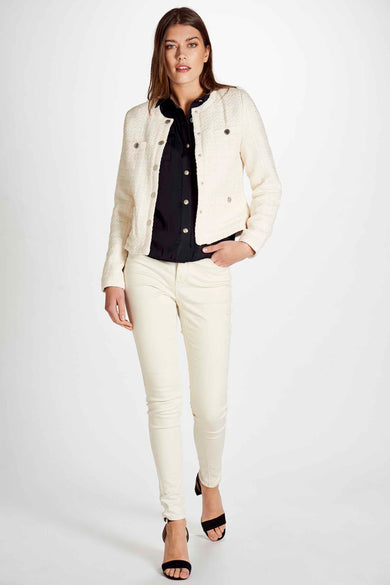 Manteau court blanc de Morgan De Toi, avec des boutons argentés, porté sur une blouse noire et un pantalon crème avec des sandales noires.