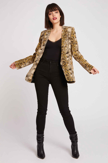 Multikleurige blazer van Morgan De Toi, met slangenprintpatroon, gecombineerd met een zwarte top, zwarte broek en zwarte laarzen.