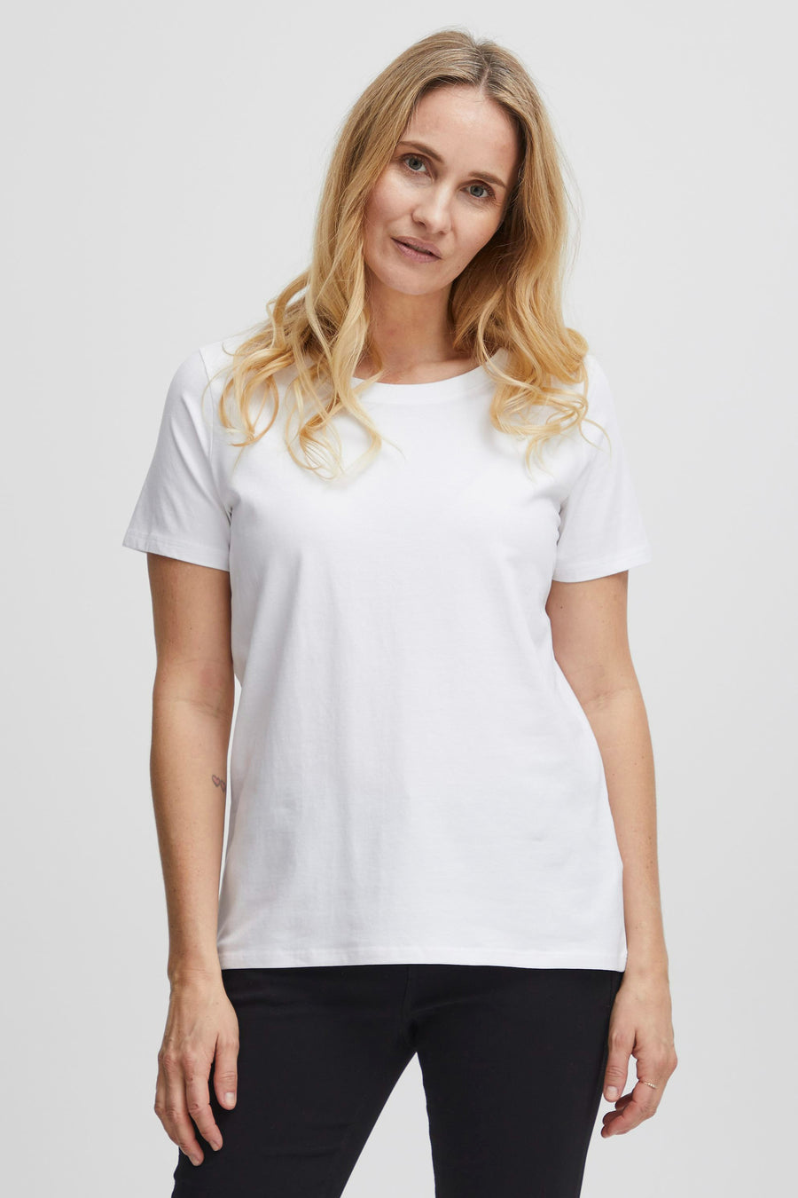 Wit T-shirt van Fransa, gedragen met zwarte broek en een subtiele tattoo op de arm.