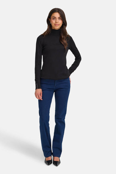 Zwarte trui met rolkraag van Fransa, met lange mouwen en een knoopdetail op de manchetten, gecombineerd met donkerblauwe jeans en zwarte pumps.

