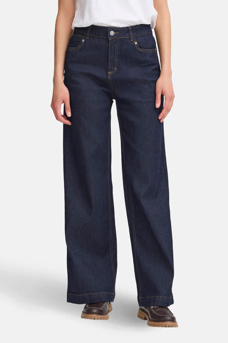 Jean bleu marine large de France, avec des boutons jaunes et des chaussures marron.