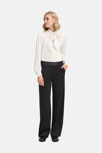 Ecru blouse met lange mouwen van Fransa, met strikdetail en gedragen met een zwarte pantalon.
