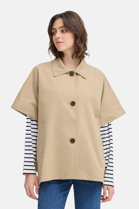Beige jas van Fransa, met knoopsluiting en korte mouwen, gecombineerd met een gestreepte top en blauwe jeans.
