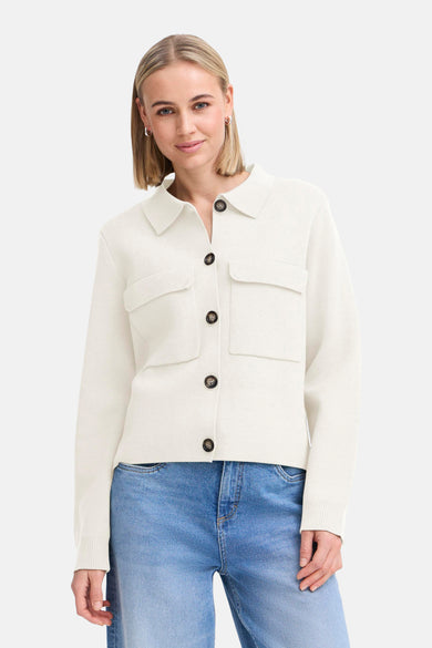 Gilet écru de France, avec des boutons bruns et des poches brodées, associé à des jeans bleus et des escarpins.