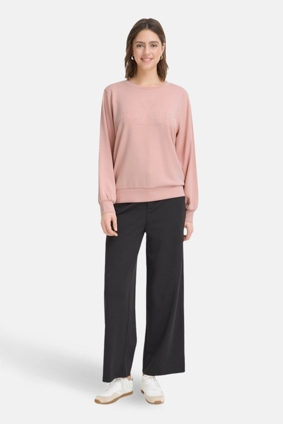 Vrouw in roze trui en zwarte broek, staand.