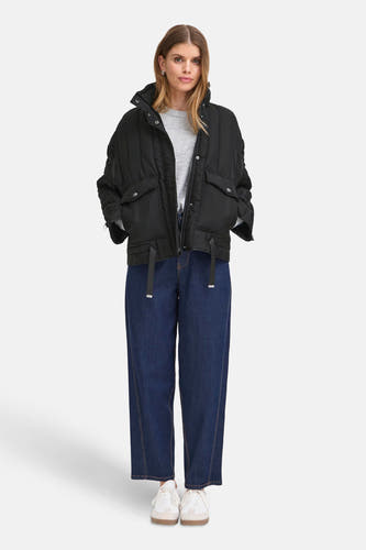 Manteau court noir de France, avec des poches et porté avec un pull gris et un jeans bleu.