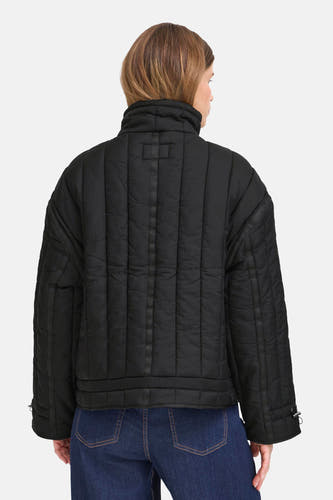 Manteau court noir de France, avec des détails brodés et porté avec un pantalon de cuir noir.