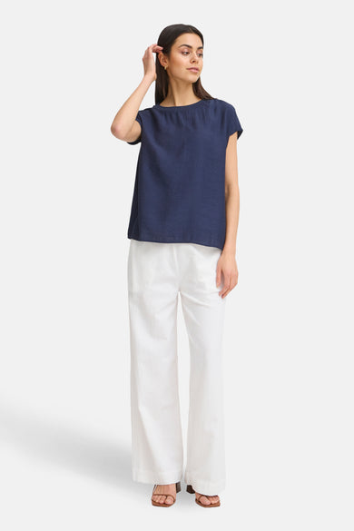Blauwe blouse met korte mouwen van Fransa, gedragen met witte, wijde broek en sandalen.
