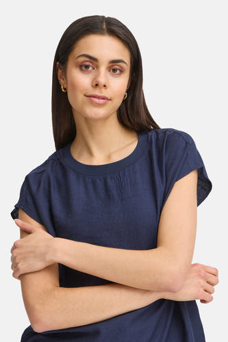 Blauwe blouse met korte mouwen van Fransa, effen textuur en met gekruiste armen gedragen.
