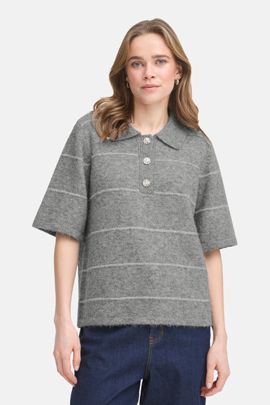 Grijze trui met V-hals van Fransa, met horizontale strepen en decoratieve knopen; gedragen met een donkere jeans.
