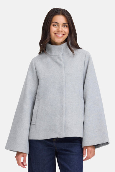 Grijze korte jas van Fransa, met wijde mouwen en een opstaande kraag, gedragen met een donkerblauwe jeans.
