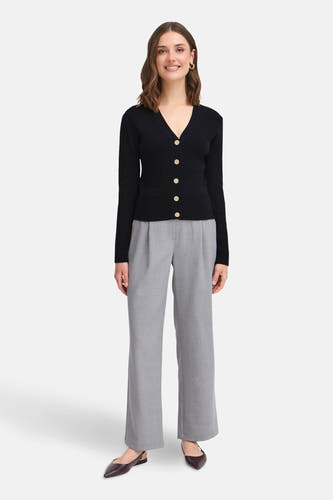 Cardigan noir de France, avec des boutons dorés et porté avec un pantalon gris et des chaussures sombres.