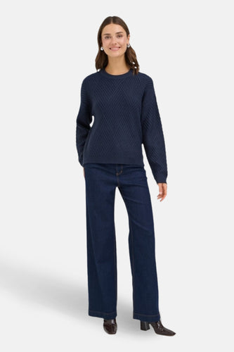 Donkerblauwe trui met ronde hals van Fransa, met diagonaal kabelpatroon en lange wijde pijpen jeans.
