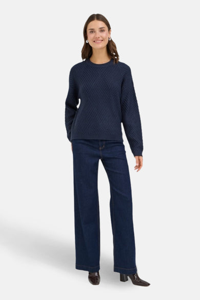 Donkerblauwe trui met ronde hals van Fransa, met diagonaal kabelpatroon en lange wijde pijpen jeans.

