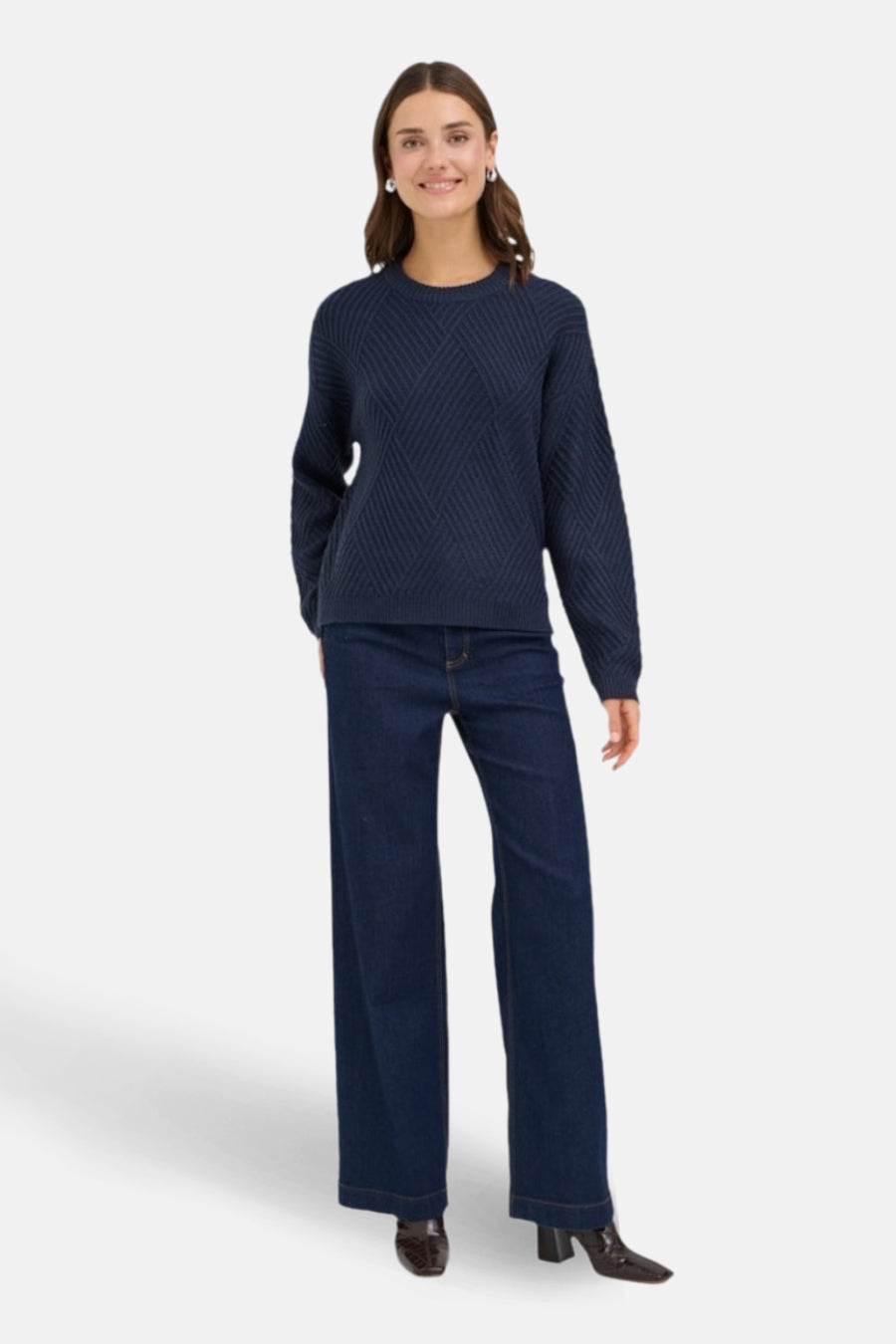 Donkerblauwe trui met ronde hals van Fransa, met diagonaal kabelpatroon en lange wijde pijpen jeans.
