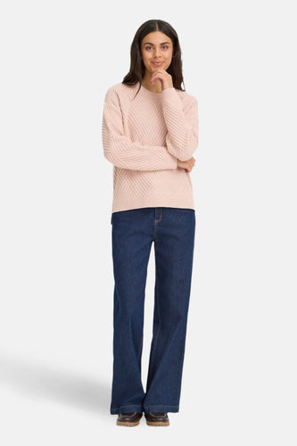 Roze trui met ronde hals van Fransa®, met een fijn geribbeld diagonaal patroon, gecombineerd met donkerblauwe jeans en bruine schoenen.
