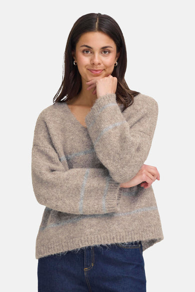 Gilet beige à col V de France, avec des rayures horizontales et des longues manches, associé à un jean foncé.