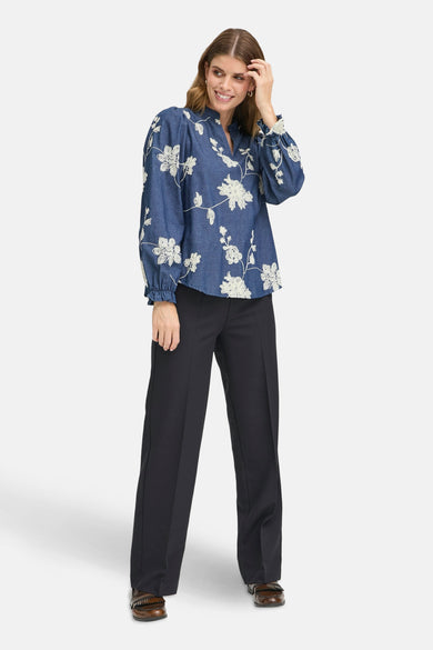 Blouse bleue à longues manches en France, avec des motifs de fleurs blanches, associée à un pantalon noir et des chaussures marron.