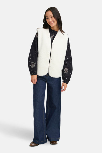 Ecru gilet van Fransa, gedragen over een zwarte blouse met dessin en donkerblauwe, wijd uitlopende jeans.
