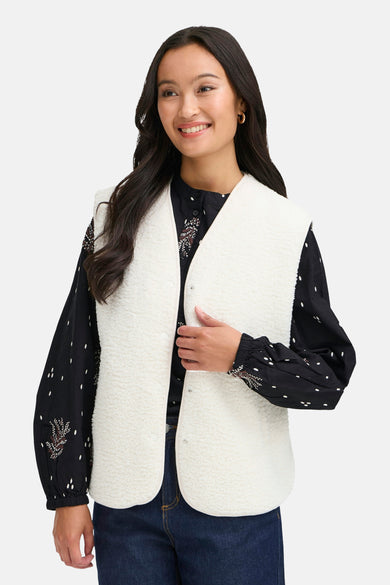 Ecru gilet van Fransa, gecombineerd met een zwarte blouse met stippen en donkere jeans.
