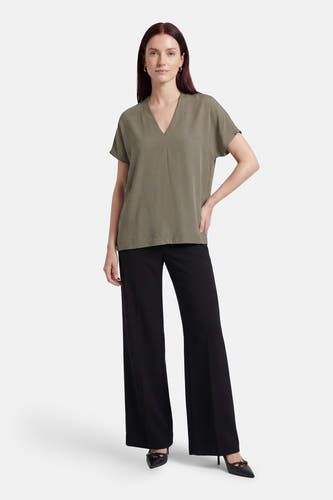 Kaki blouse met korte mouwen van Fransa, gecombineerd met zwarte, wijde broek en zwarte pumps.