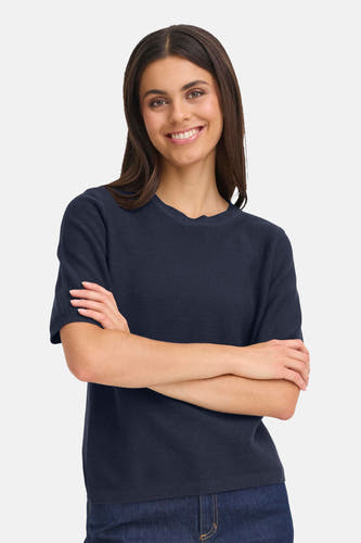 Pull bleu avec col rond de France, associé à des jeans foncés et des chaussures pointues.