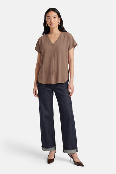 Beige blouse met korte mouwen van Fransa, met V-hals en gedragen met donkere jeans en hakken.
