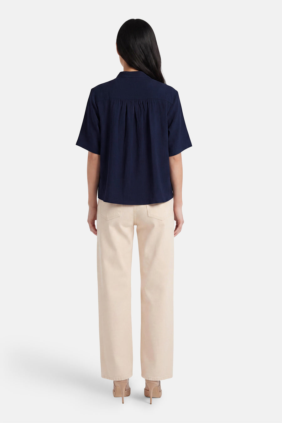 Chemise bleue à manches courtes de Fransa®, avec plis au dos, vue de dos sur mannequin portant un pantalon clair et des talons.