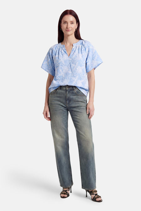 Blauwe blouse met korte mouwen van Fransa® met wit bloemenborduursel, V-hals, gecombineerd met jeans en zwarte hakken.