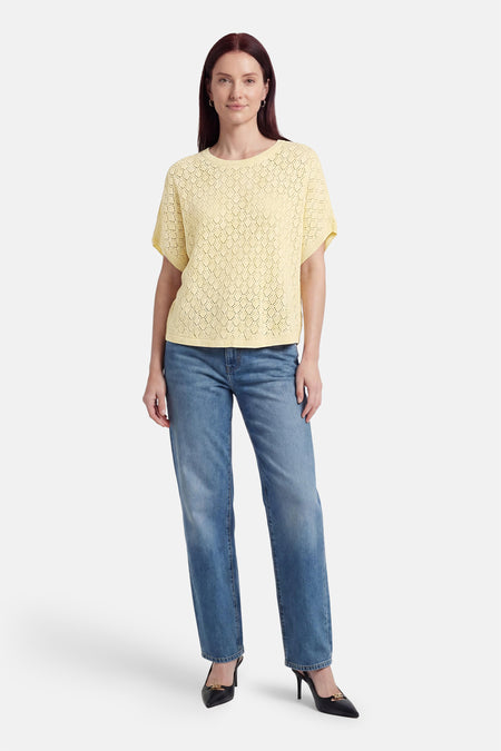 Gele pull met ronde hals van Fransa, met ajourpatroon, korte mouwen, gedragen met jeans en zwarte hakken.