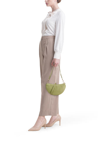 Groene dames crossbody tas van Access®, halvemaanvormig, van gestructureerd leer, gedragen door model met witte blouse en beige broek.