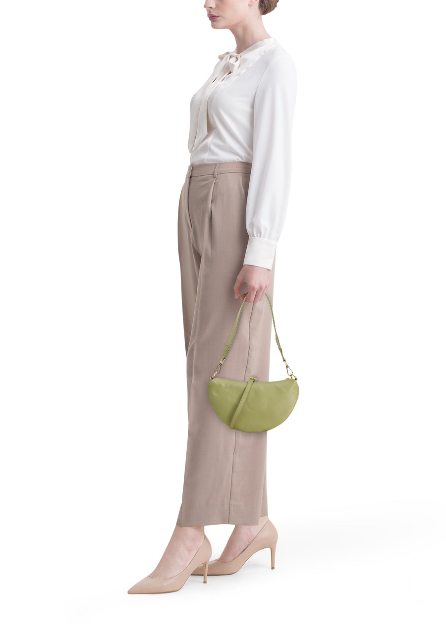 Groene dames crossbody tas van Access®, halvemaanvormig, van gestructureerd leer, gedragen door model met witte blouse en beige broek.