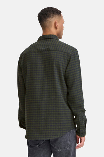 Achterkant van een man in een geruit groen en donkerblauw overhemd en grijze jeans.