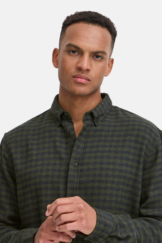 Een man in een olijfgroen geruit overhemd met lange mouwen.