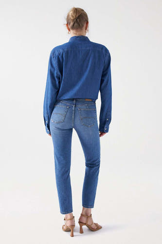 Lichtblauwe slim jeans van Salsa Jeans, gezien van achteren, gecombineerd met een denim blouse en hoge hakken.