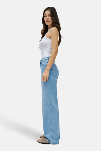 Wijde jeans van lichtblauw denim van Salsa Jeans, gezien van opzij, met een wit hemdje en sandalen.
