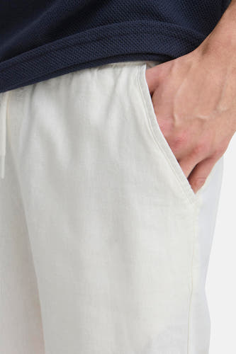 Short bleu de SOLID, ici représenté en tissu lin blanc avec une main dans la poche latérale.