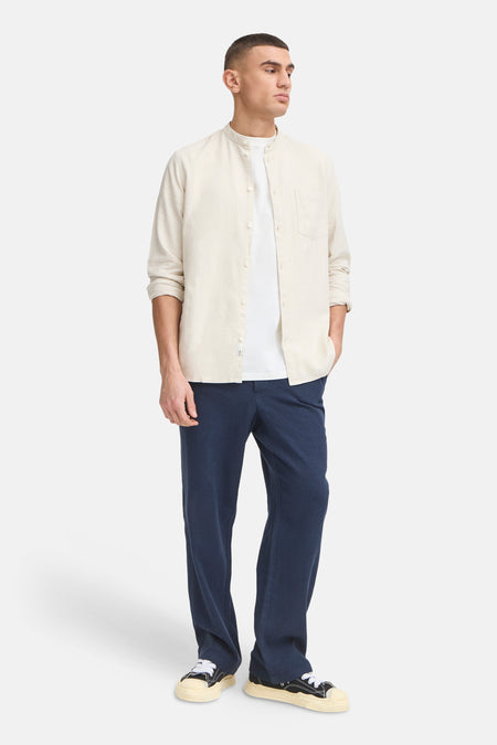Blauwe broek van SOLID, met een losse pasvorm en gedragen met een wit T-shirt en overhemd.
