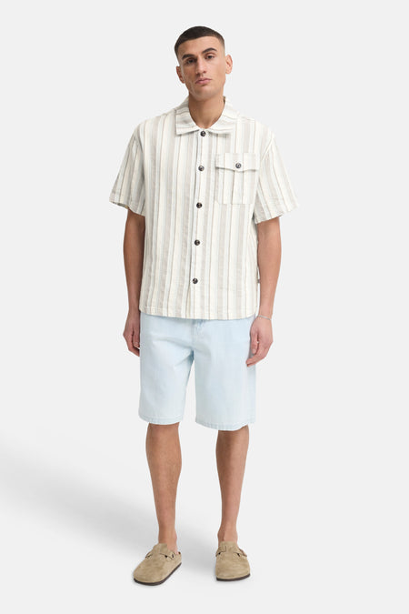 Gestreepte kortemouw hemd in beige en wit van SOLID, met revere kraag en borstzak, gedragen met lichtblauwe shorts en suède klompen.